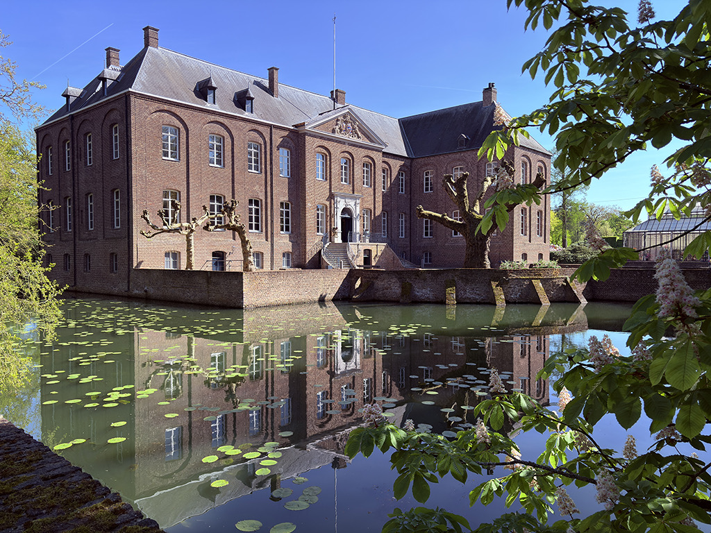 Statig kasteel weerspiegeld in de slotgracht op de Kasteeltuinen-route in Noord-Limburg