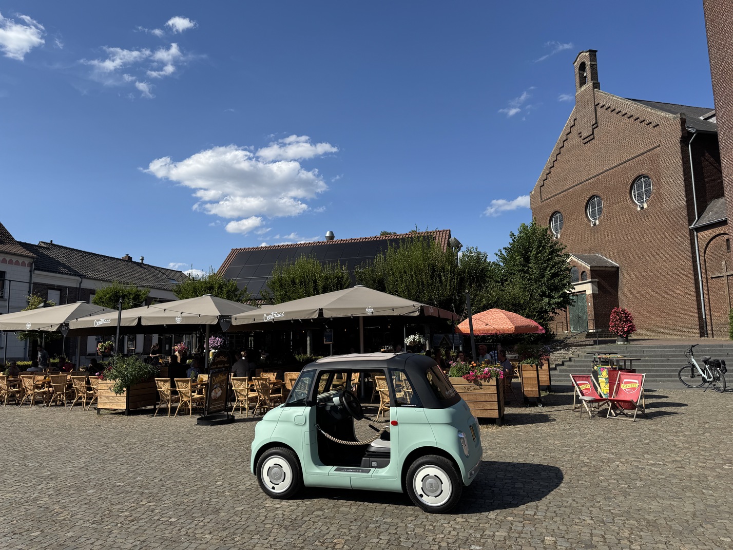 Fiat Topolino op het dorpsplein bij terras Centraal in Baarlo, met de kerk op de achtergrond